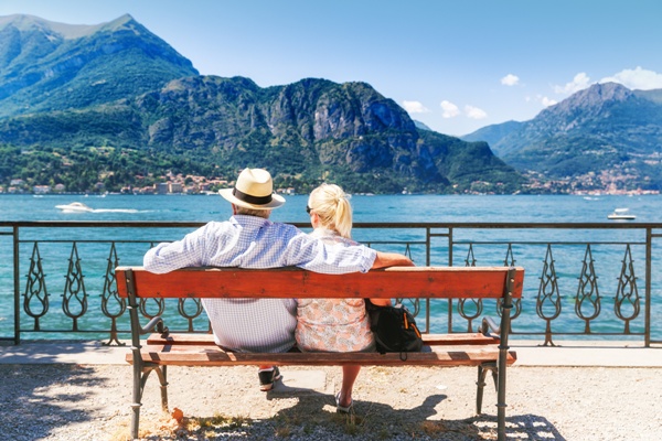 Lake Como, village Bellagio, Italy. Senior couple weekend getaway having rest on the bench by spectacular lake Como in Italy. Sunny day scenery. Tourists admiring view on popular tourist attraction.